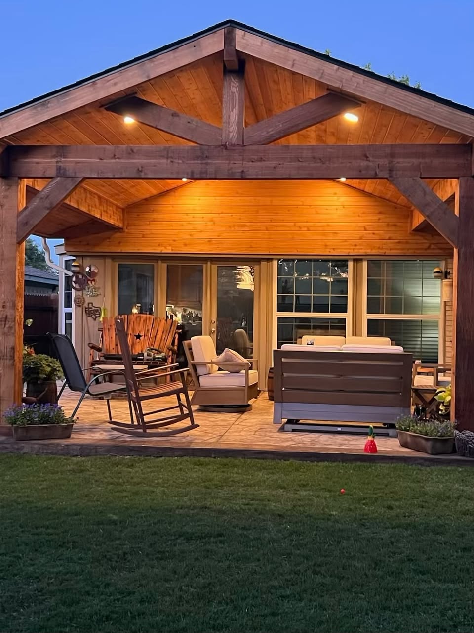 Cedar gable patio cover with exposed trusses, lantern lights and a stone outdoor kitchen