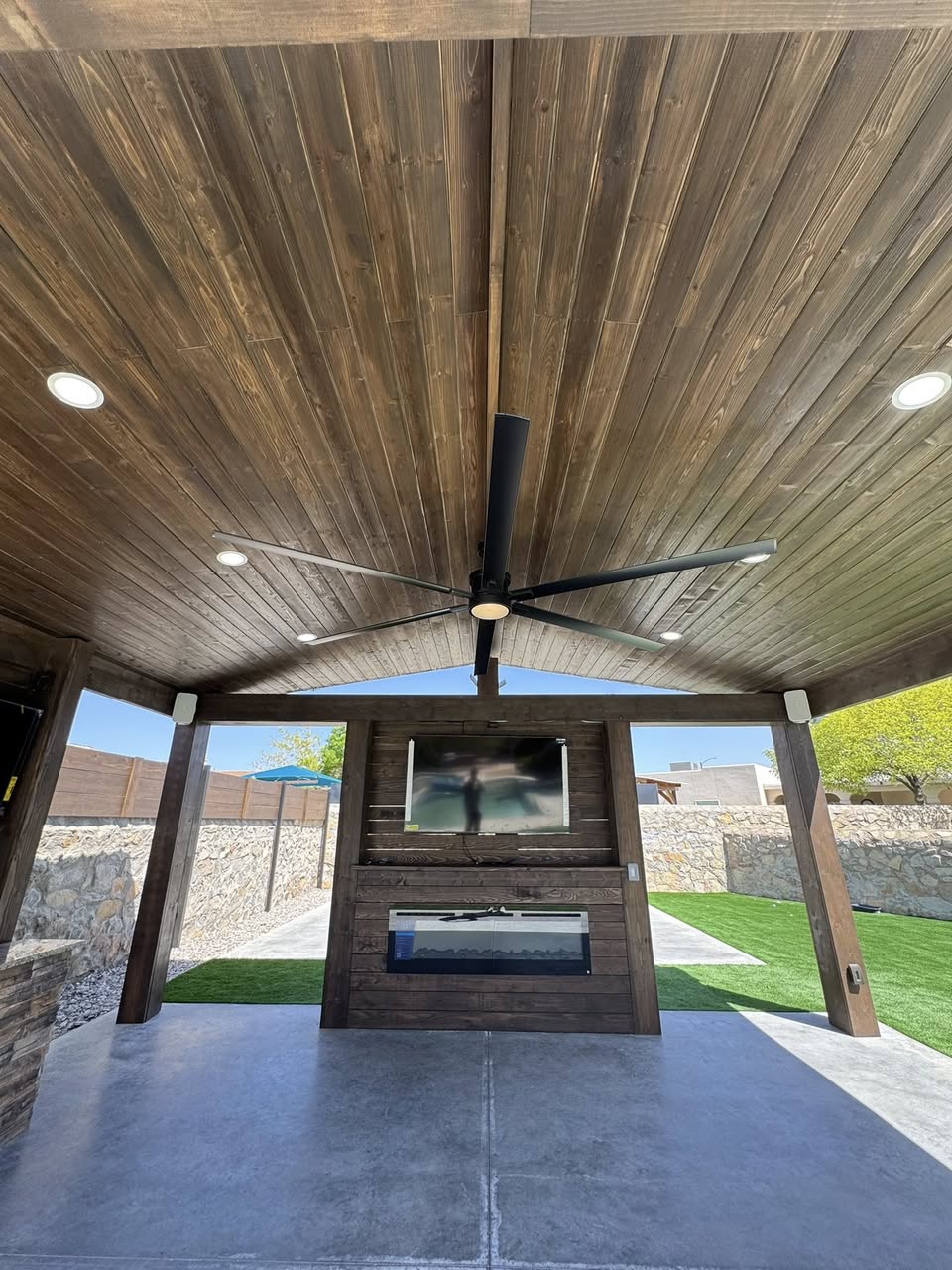 Gable-roof patio cover with stained wood ceiling and recessed lighting attached to a San Antonio home at dusk