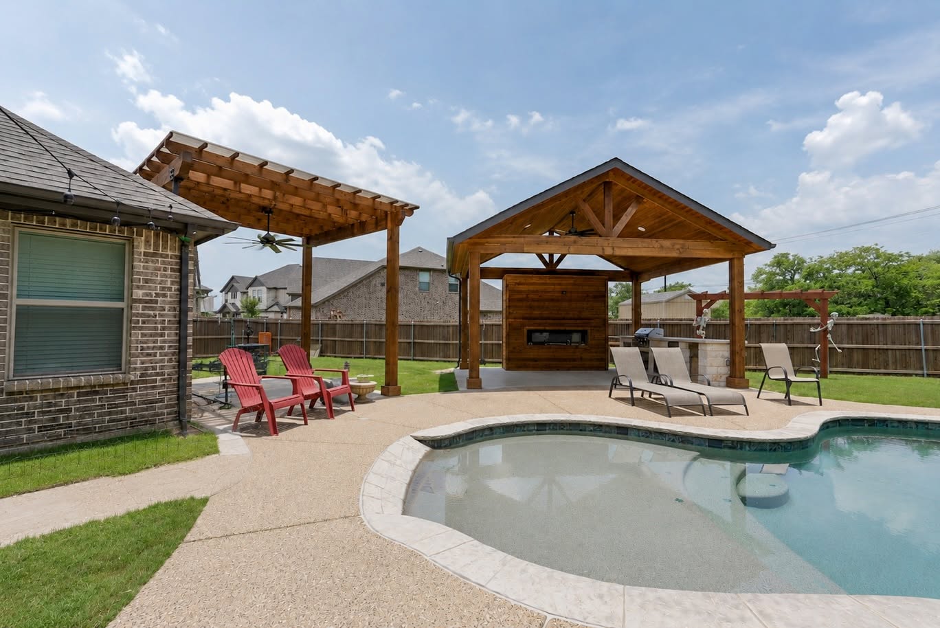 Freestanding cedar pavilion with fireplace and outdoor kitchen beside a backyard pool